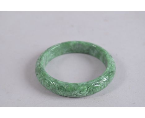 A CARVED GREEN JADE BANGLE. 3ins diameter.