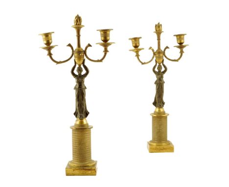 A pair of Empire style gilt and patinated bronze figural candlesticks, each with a flaming finial above a pair of engine turn