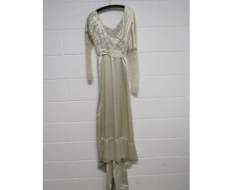 A 1910 cream satin bridal gown embroidered with pale green floral detail at the bodice laced sleeves, large covered button de