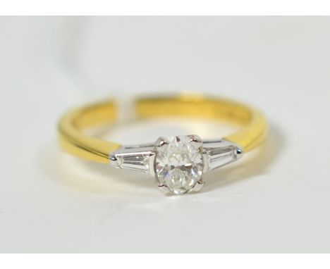 An 18 carat gold diamond ring, an oval cut diamond to tapered baguette cut diamond set shoulders, total estimated diamond wei