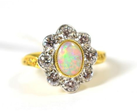 An 18 carat gold opal and diamond cluster ring, an oval cabochon opal in a milgrain setting, within a border of round brillia