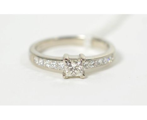 A platinum princess cut solitaire diamond ring, in a claw setting, to channel set princess cut diamond set shoulders, total e