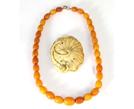 An amber bead necklace, graduated oval beads knotted to a jump ring, length 44cm and a carved Japanese lotus leaf (2) .  Ambe