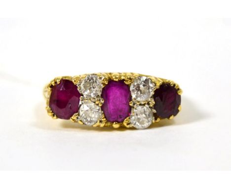 An 18 carat gold ruby and diamond ring, three graduated oval cut rubies spaced by pairs of old cut diamonds, to a carved shan