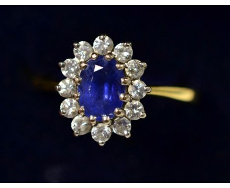 An 18 carat gold sapphire and diamond cluster ring, an oval cut sapphire within a border of round brilliant cut diamonds, to 