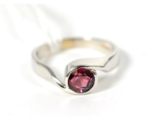 An 18 carat white gold garnet ring, a round cut garnet in a rubbed over setting, to bypass scroll shoulders, finger size O1/2