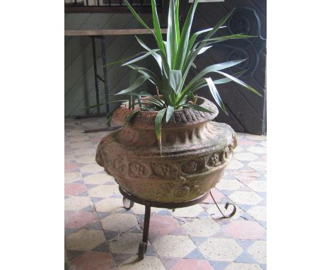 A weathered terracotta planter of circular form with repeating flower head detail, raised on an ironwork frame, 60cm diameter