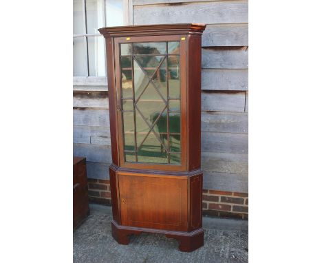 A mahogany two-section corner display cabinet, the upper section enclosed astragal glazed door over panelled door, on bracket