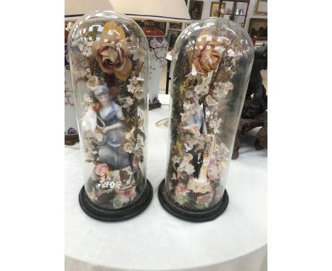 A pair of glass domes containing ceramic fishers and floral surrounds