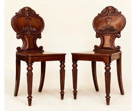 HALL CHAIRS, a pair, Regency period mahogany each with scroll carved rounded backs, panel seats and turned front supports, 41