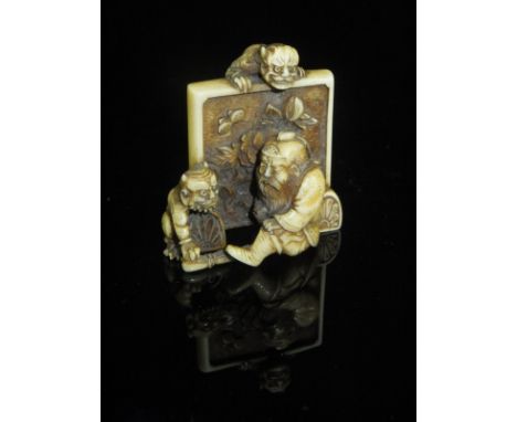 A 19th Century Japanese Meiji Period carved ivory netsuke in the form of a bearded gentleman seated by a floral decorated scr