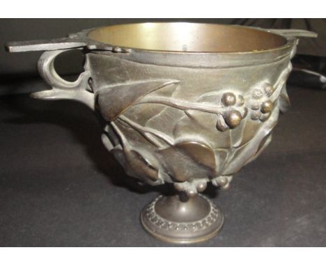 A Victorian bronze trophy cup with heavy relief work, ivy and berry decoration, all flanked by two handles raised upon a circ