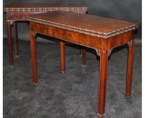 A pair of George III mahogany card tables in the manner of Thomas Chippendale, the plain fold-over tops with flower head carv