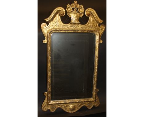 An early 18th Century giltwood and gesso wall mirror, the broken arch top with basket of flowers finial over a bevel edged pl