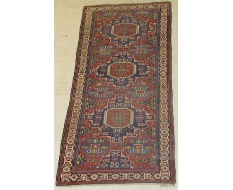 A Caucasian rug, the central panel set with three repeating geometric patterned medallions on an elephant foot decorated red 