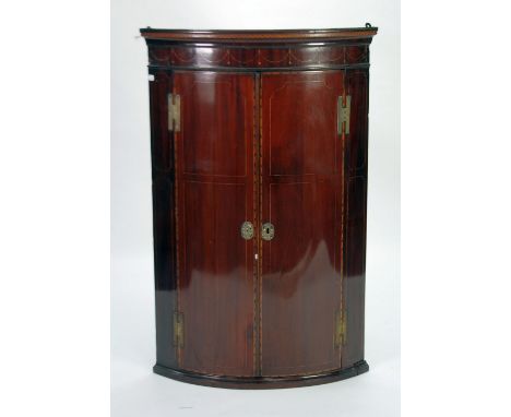 GEORGE III INLAID MAHOGANY BOW FRONTED CORNER CUPBOARD, the moulded cornice above a pendant inlaid frieze and pair of cupboar