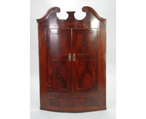 EARLY NINETEENTH CENTURY FIGURED MAHOGANY AND ROSEWOOD CROSSBANDED BOW FRONTED CORNER CUPBOARD, the swan neck cornice above a