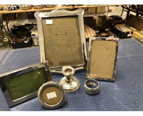 Four easel back hallmarked silver photo frames, a silver napkin ring and a loaded dwarf candlestick. 
