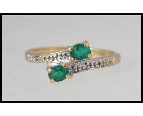 A 9ct gold cross over ring set with two oval cut emeralds and illusion set diamonds. Hallmarked Birmingham with CCM mark. Siz