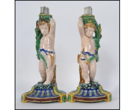 A pair of Minton Majolica figural candlesticks modelled as cherubs raised on naturalistic socle plinth bases  Impressed Minto