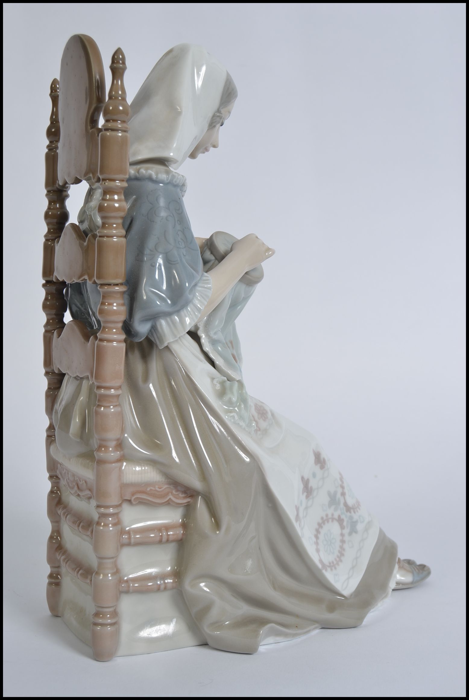 A large Lladro figurine of a seated lady sewing a tapestry. CONDITION