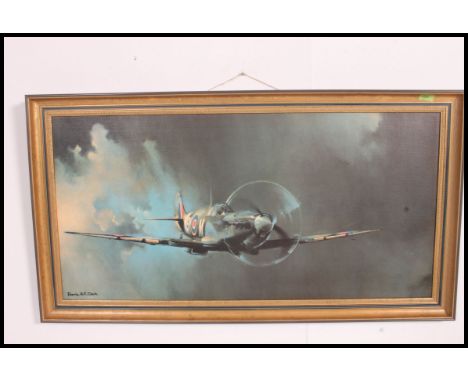 A large framed print of a spitfire in clouded sky being signed to the corner by Barrie Clark 100x50