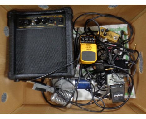 A box containing a G-10 guitar amplifier, microphones and Behringer and Daphon guitar effects pedals.