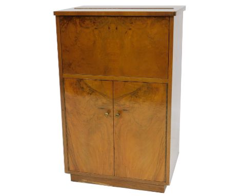 An Art Deco walnut cocktail cabinet, with a hinged top and drop down front, enclosing a small glass shelf above a pair of cup