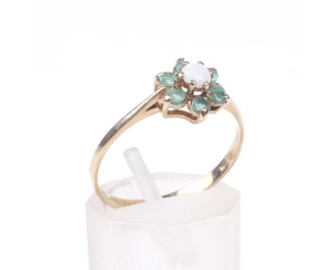 A 9ct gold, opal and emerald cluster dress ring. The central round cabochon white opal displays a muted play of colours, with