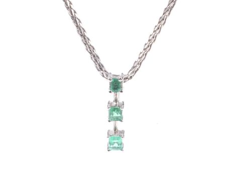 An emerald three stone pendant and chain. The white metal pendant claw set with three graduated emerald-cut and square step-c