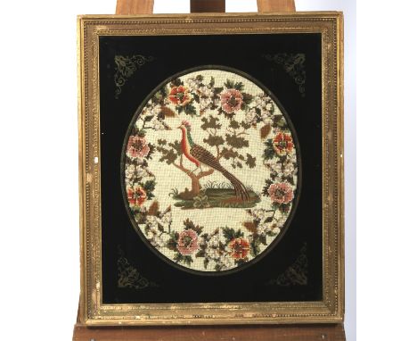A Victorian needlework in verre eglomise giltwood frame. Worked with a tapestry exotic bird perched on a tree within floral g