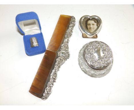 A silver top dressing table jar, a comb, a small heart-shaped photo frame and a thimble. (4)