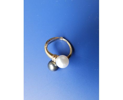 A modern crossover style yellow metal ring set with a white pearl & a black pearl.