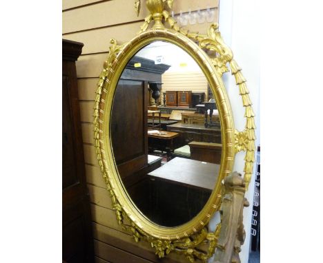 A REGENCY STYLE GILT DECORATED OVAL WALL MIRROR with flame topped urn finial and open swag and ribbon decoration, 117 x 68 cm