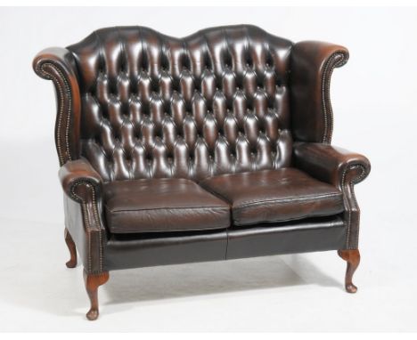 A mid-20th century tan leather wing back settee
With a twin arched button back above cylindrical padded arms and cushion seat