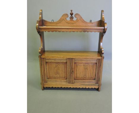 A late Victorian walnut hanging wall cabinet, incorporating a shelf with pendent frieze above a pair of panel cupboard doors,