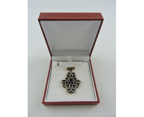A sapphire pendant, set in a white metal and gilded strapwork frame, on a fine chain, 17g.