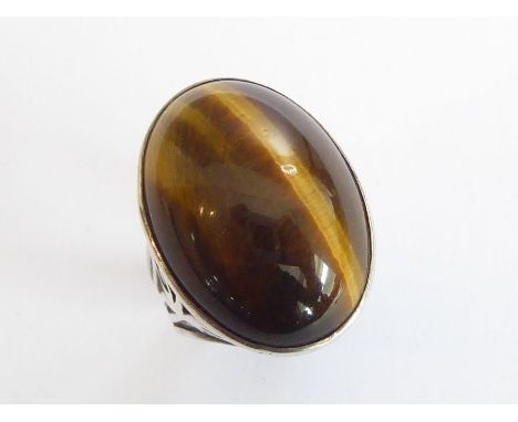 A large, heavy and striking 1970s dress ring; custom-made with centrally set vertical cabochon tiger's eye, the pierced, hall