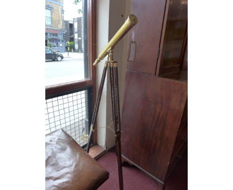 A brass telescope raised on adjustable wooden tripod supports. 
