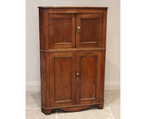 A late George III oak freestanding corner cupboard, formed as two pairs of panelled cupboard doors, each applied with brass k