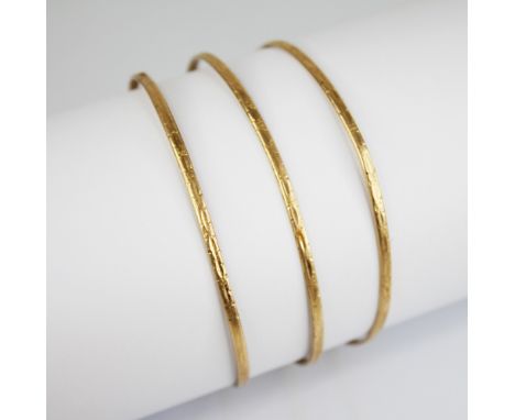 Three gold coloured bangles, each of circular form with engine turned decoration to the exterior, stamped ?18K? interior, 2mm
