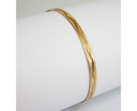 A gold coloured bangle, of oval form with engine turned decoration to exterior, stamped ?18K? to interior, 4mm wide, max. wid