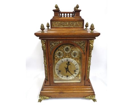 A large oak cased bracket clock, brass face with raised ornate detailing, silvered chapter ring with Roman numerals and outer
