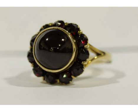 A gold and cabochon garnet cluster ring, set with large central 9.5mm cabochon garnet, surrounded by smaller facetted garnets