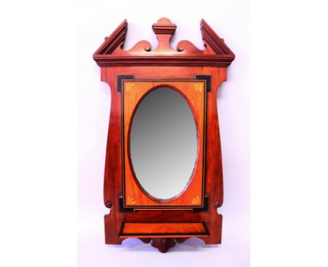 AN EDWARDIAN MAHOGANY FRAMED OVAL MIRROR with bevelled edge, broken arched pediment and small shelf. 2'10"ft long, 1ft 7ins w