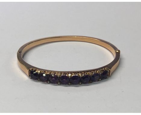 An Edwardian yellow metal half hinged oval bangle set with eight claw-set circular amethysts with small seed pearls at each c