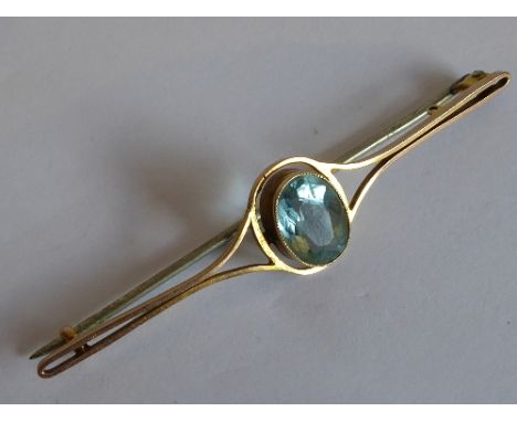 A yellow metal stick brooch centrally set with an oval hand-cut tourmaline 