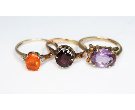 A group of three rings comprising one set with an orange fire opal, one with a garnet and the other an amethyst, various 9ct 