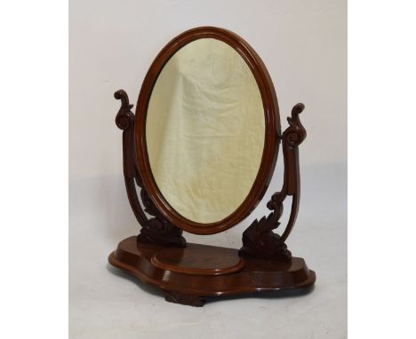 Victorian mahogany swing dressing mirror, the plain oval plate within moulded frame between foliate-carved scroll supports on