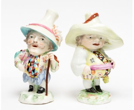 A pair of Derby Mansion House dwarfs, circa 1760, each modelled standing wearing oversized hats, one holding a staff, both we